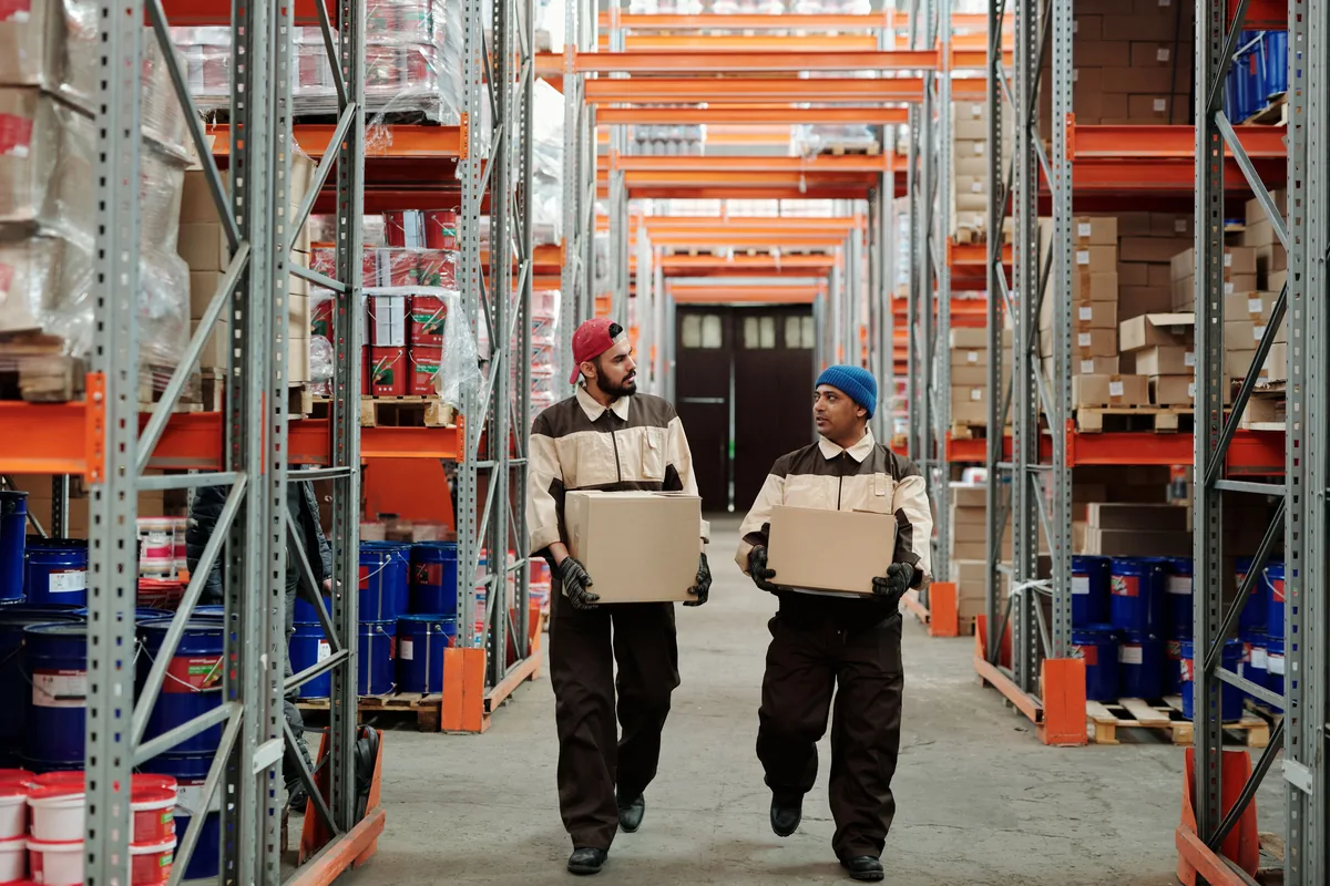 Twee collega's dragen dozen in een magazijn.