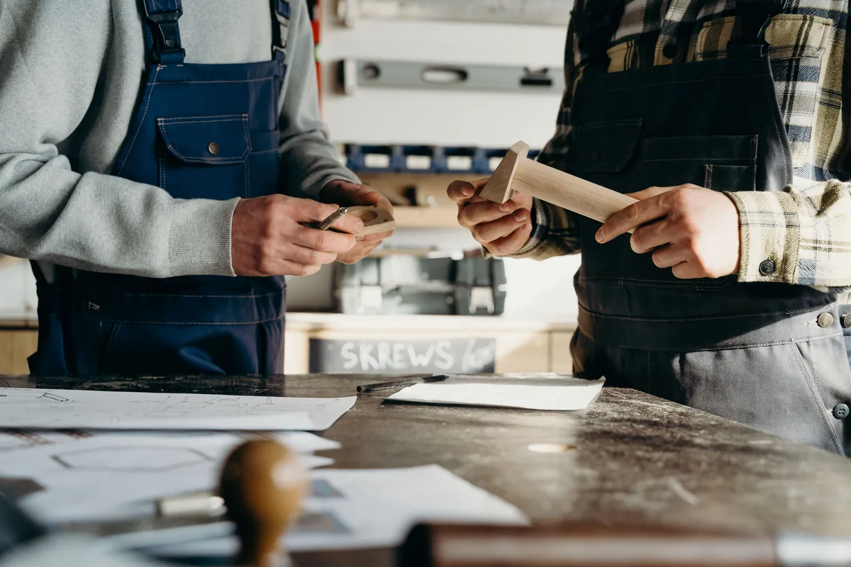 Twee vakmensen in werkkleding werken samen aan een houten werkstuk.